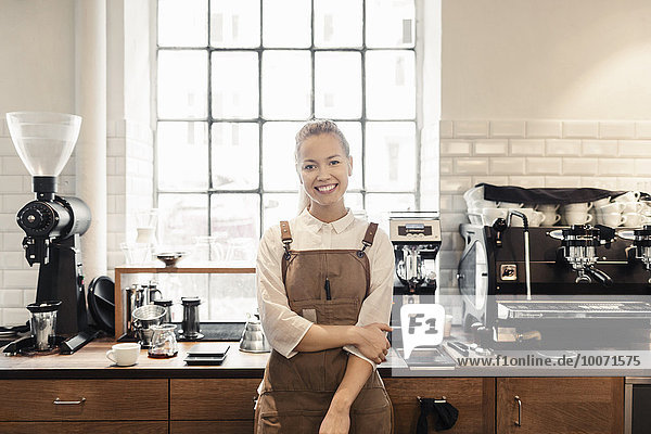 Portrait of happy female barista standing by counter in coffee shop