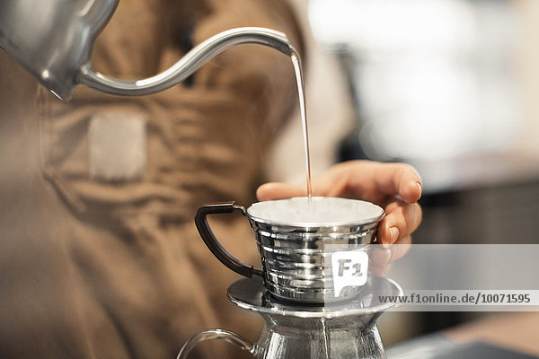 Abgeschnittenes Bild eines Barista  der Wasser in eine Kaffeetasse im Cafe gießt.