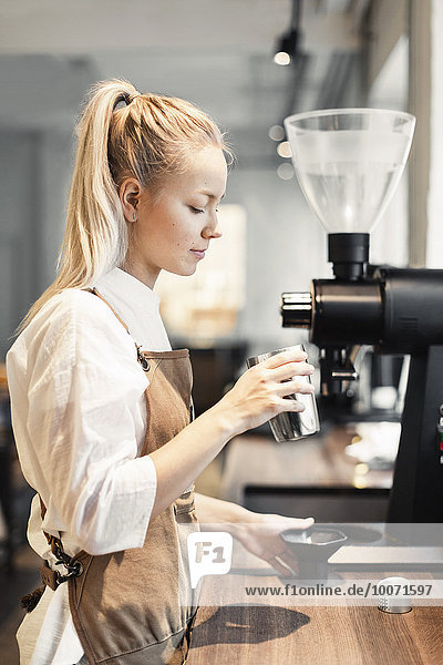 Seitenansicht des weiblichen Barista-Behälters bei der Kaffeemaschine am Tresen im Cafe