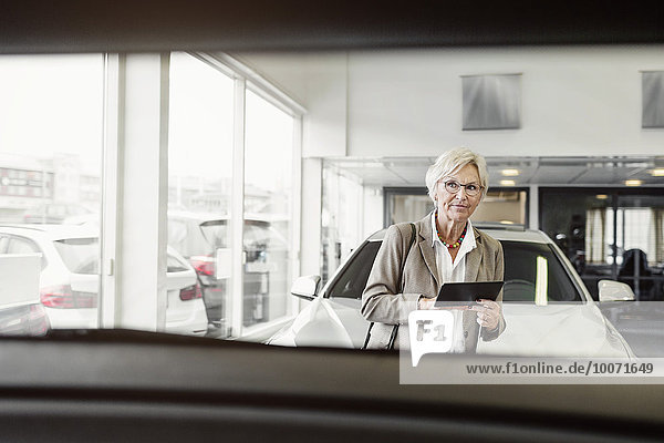 Senior Geschäftsfrau mit digitalem Tablett beim Blick auf das Auto im Geschäft
