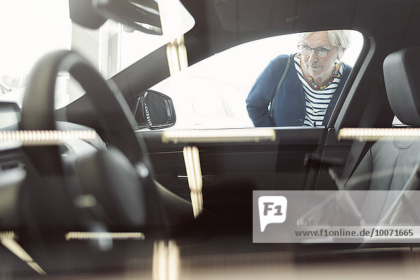 Seniorin bewunderndes Auto im Laden ausgestellt