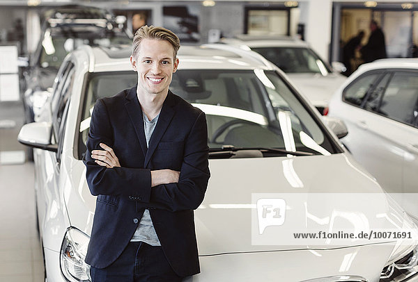 Porträt eines glücklichen  männlichen Kunden  der sich im Showroom auf das Auto stützt.