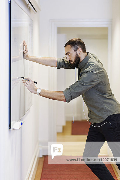 Side view of businessman writing on whiteboard in office