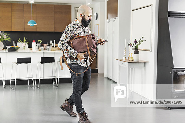 Volle Länge des männlichen Architekten mit Tasche mit Handy beim Gehen in der Küche