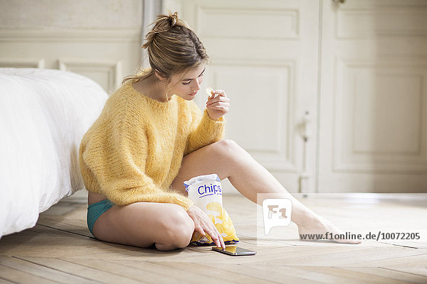 Woman using phone and eating chips