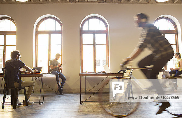 Lässiger Geschäftsmann beim Fahrradfahren im Großraumbüro