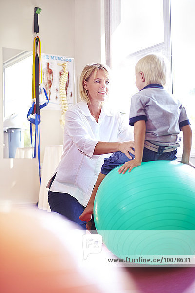Physiotherapeutin hält Junge auf Fitnessball