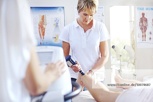Physiotherapeutin mit Ultraschallsonde am Bein der Frau