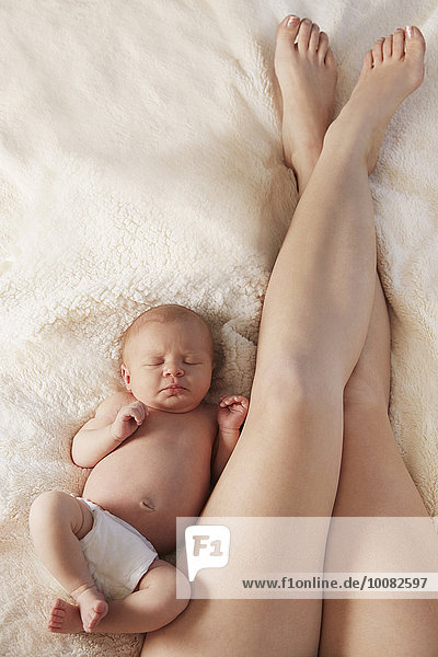 Legs of mother laying on bed with newborn baby