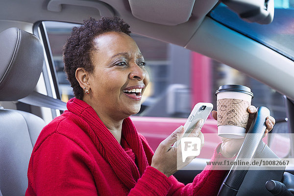 Black woman using cell phone and drinking coffee while driving car