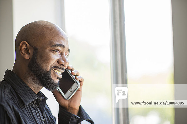 Black man talking on cell phone near window