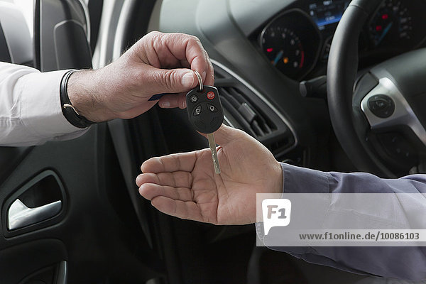 Hispanic car salesman handing keys to customer