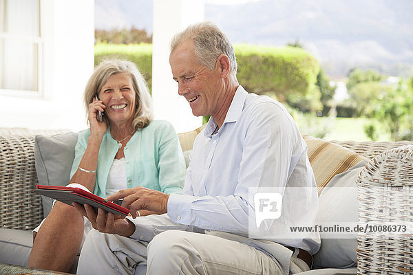 Caucasian couple using cell phone and digital tablet on sofa