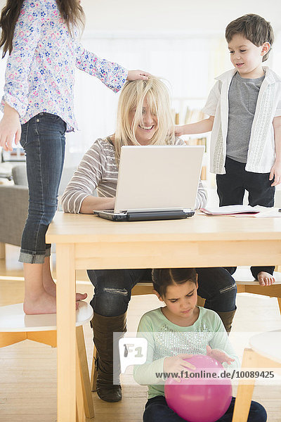 Caucasian mother using laptop with chaotic children