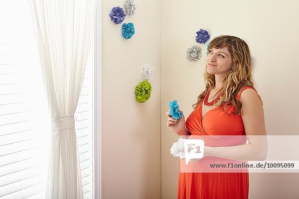 Schwangere Frau dekoriert Kinderzimmer mit Papierblumen