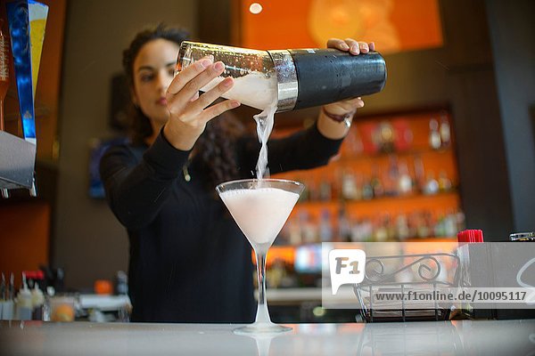 Junge Barkeeperin gießt Cocktail aus dem Shaker in die Cocktailbar