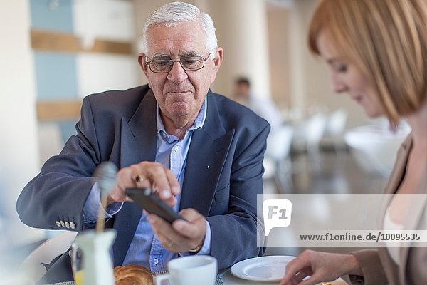 Senior businessman smartphone texting at breakfast table in hotel restaurant