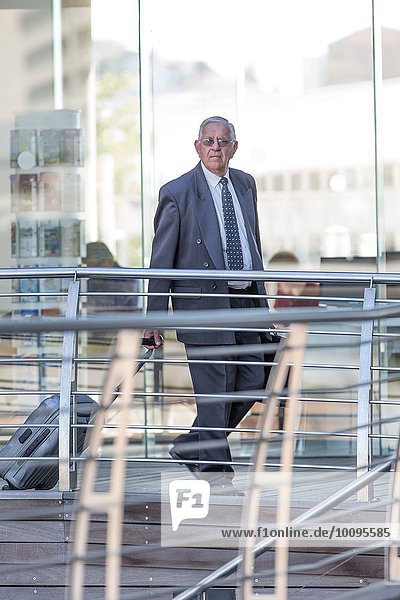 Senior businessman leaving hotel with wheeled suitcase