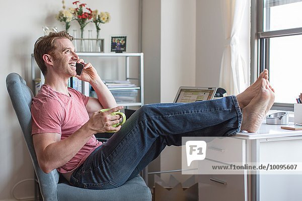 Mid adult man with feet up on desk chatting on smartphone