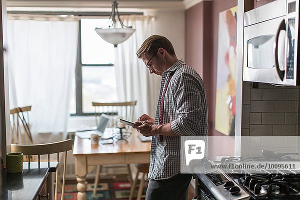 Mid adult man in kitchen using touchscreen on digital tablet