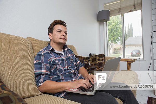 Junger Mann auf dem Sofa sitzend mit Laptop