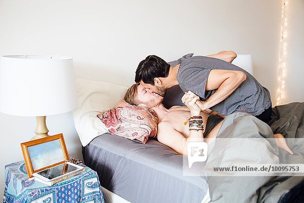 Männliches Paar auf dem Bett  Händchen haltend  küssend