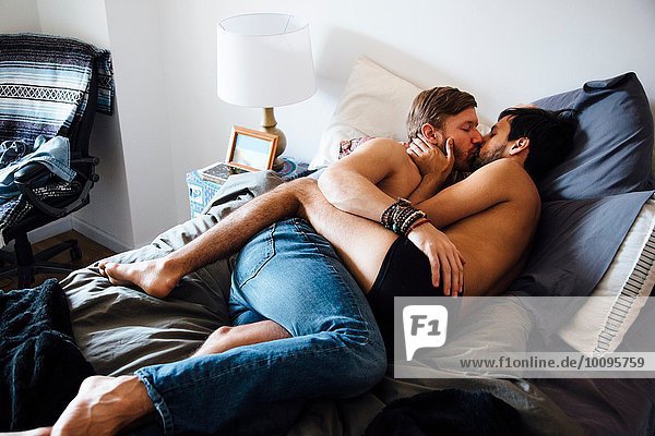 Male couple  partially dressed  lying on bed  kissing
