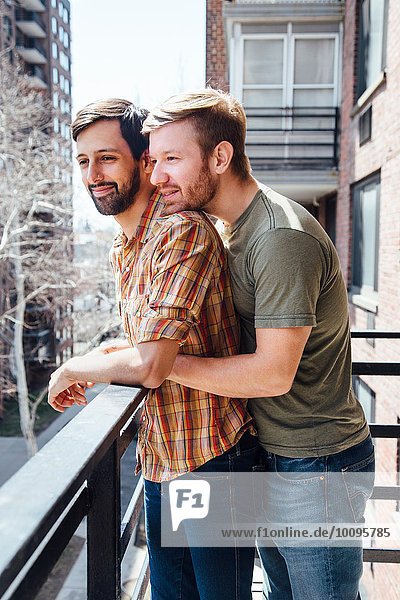 Männliches Paar auf dem Balkon stehend  mit Blick auf die Aussicht  umarmend