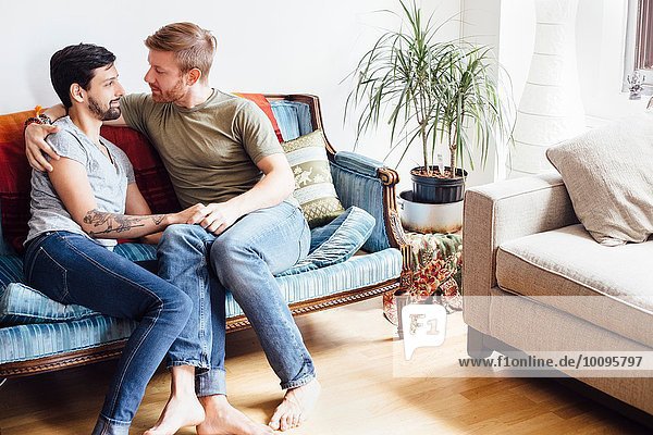 Männliches Paar auf Sofa sitzend,  umarmend,  von Angesicht zu Angesicht