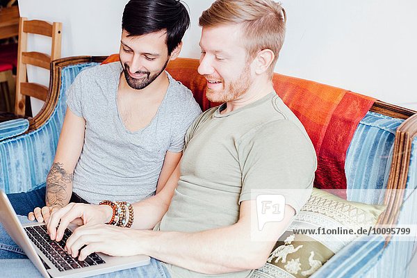 Männliches Paar auf dem Sofa sitzend  auf den Laptop schauend  lächelnd