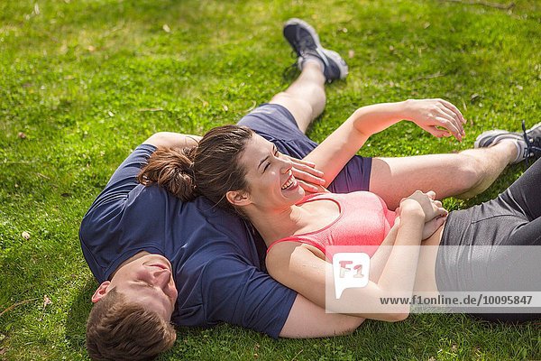 Romantic young sporty couple lying on park grass