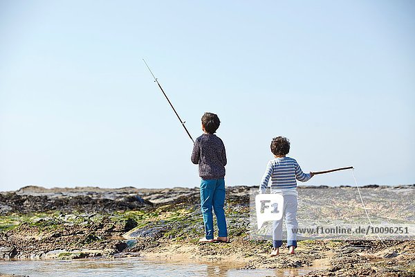 Two young boys  fishing on beach  rear view