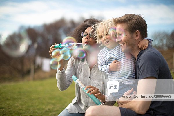 Mother blowing bubbles father holding son