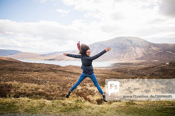 Mid adult woman in mountains doing star jump  Isle of Skye  Hebrides  Scotland