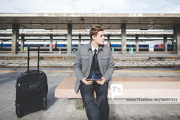 Portrait of young businessman commuter using digital tablet at train station.