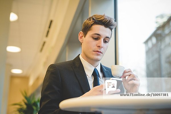 Portrait of young businessman sitting in cafe using digital tablet and mobile phone.