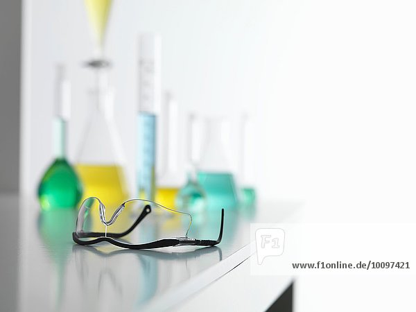 Schutzbrille auf dem Labortisch mit einem chemischen Experiment im Hintergrund