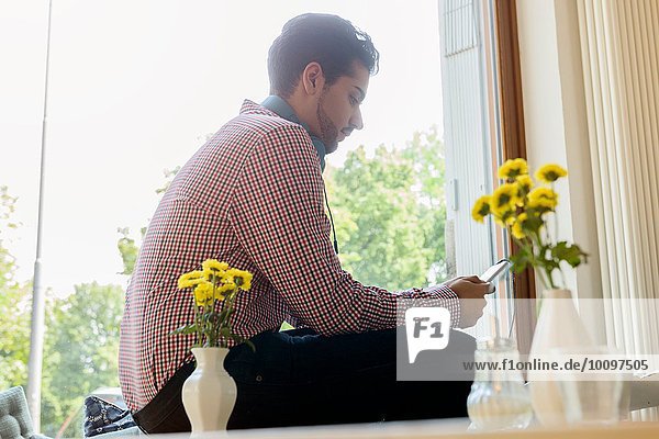 Young man in cafe window seat selecting music on smartphone
