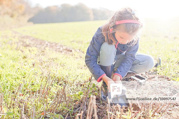 Girl with metal detector crouching and digging with spade in field