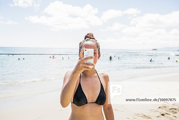 Young woman wearing bikini top taking smartphone selfie on Waikiki Beach  Hawaii  USA