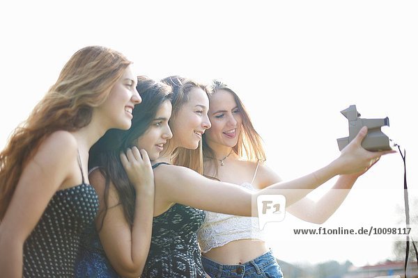 Four teenage girls taking instant camera selfie in park