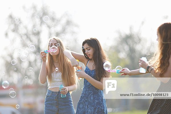 Drei Teenagermädchen beim Blasenblasen mit Blasenstab im Park