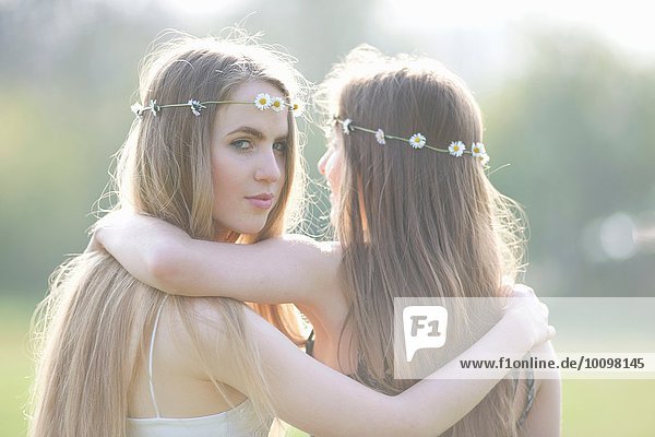 Porträt von zwei Teenagermädchen in Gänseblümchen-Kopfbedeckung im Park