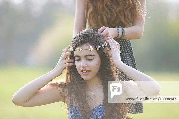 Zwei Mädchen im Teenageralter  die sich im Park Kopfbedeckungen anziehen und tragen.