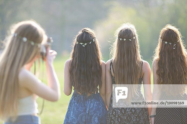 Rückansicht eines Teenagermädchens  das Freunde in Gänseblümchen-Kopfbedeckungen im Park fotografiert.