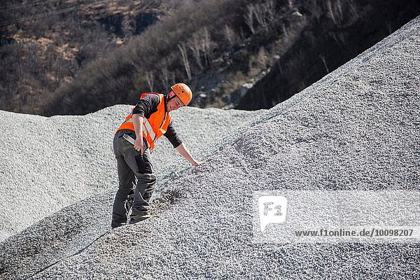 Quarry worker measuring on gravel mound at quarry