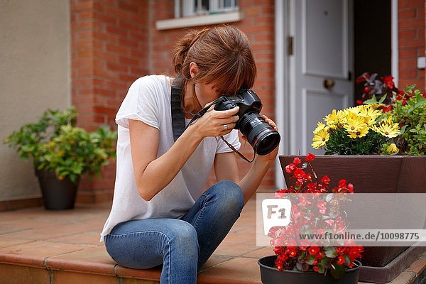 Mittlere erwachsene Frau  die im Freien sitzt und Blumentöpfe fotografiert.