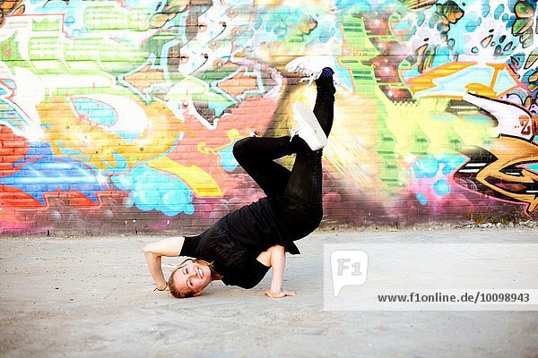 Junge Frau in auf dem Kopf stehendem Breakdance-Frost gegen Graffiti