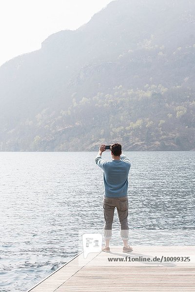 Rückansicht des jungen Mannes beim Fotografieren vom Pier  Mergozzo-See  Verbania  Piemonte  Italien
