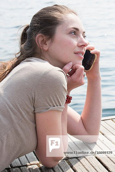 Junge Frau liegt am Pier und plaudert am Smartphone  Mergozzo-See  Verbania  Piemonte  Italien
